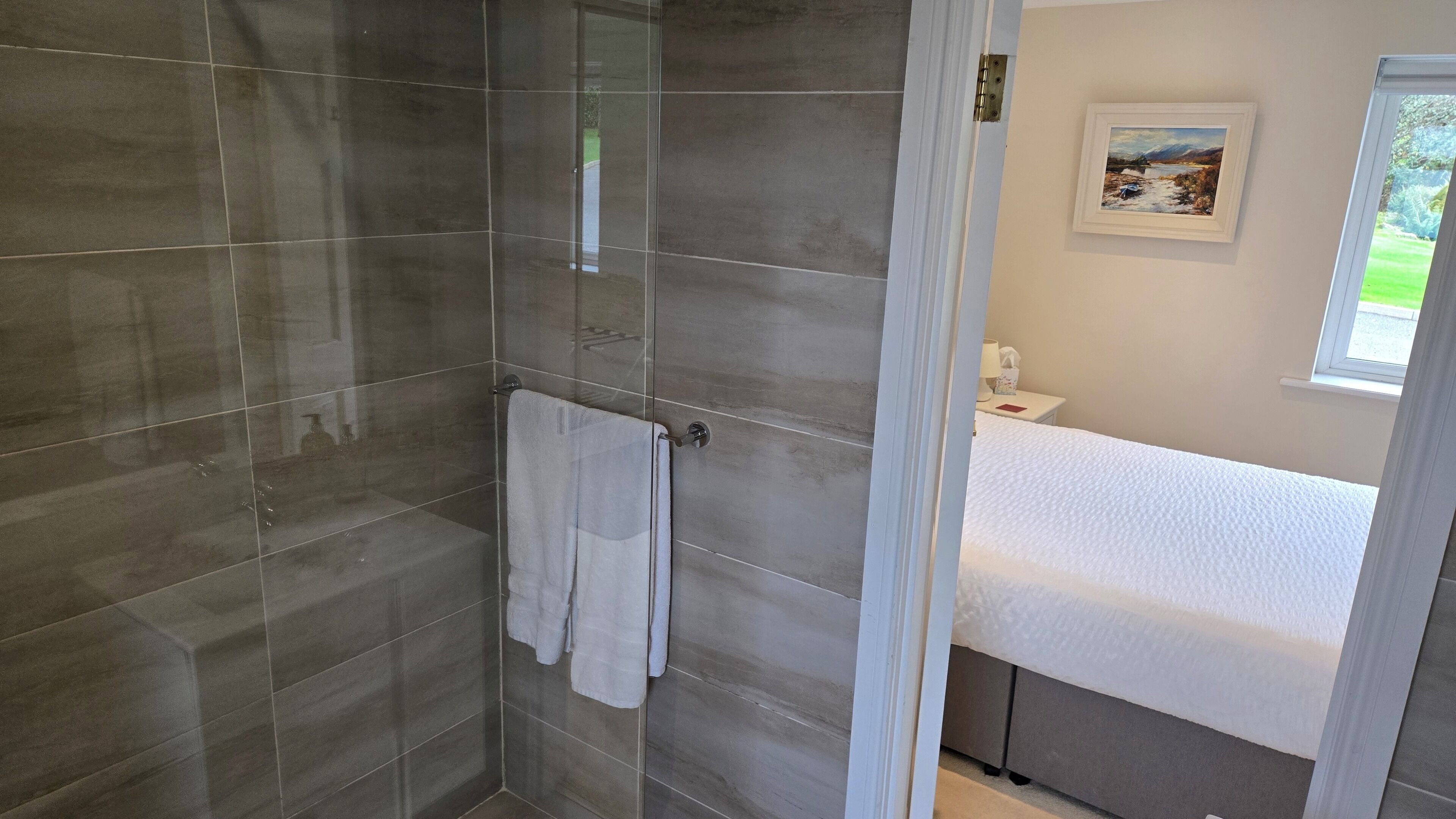 A modern bathroom with a glass shower enclosure, a white sink, and a framed landscape painting on the wall.