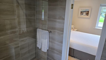 Un baño moderno con cabina de ducha de vidrio, un lavabo blanco y un cuadro de paisaje enmarcado en la pared.