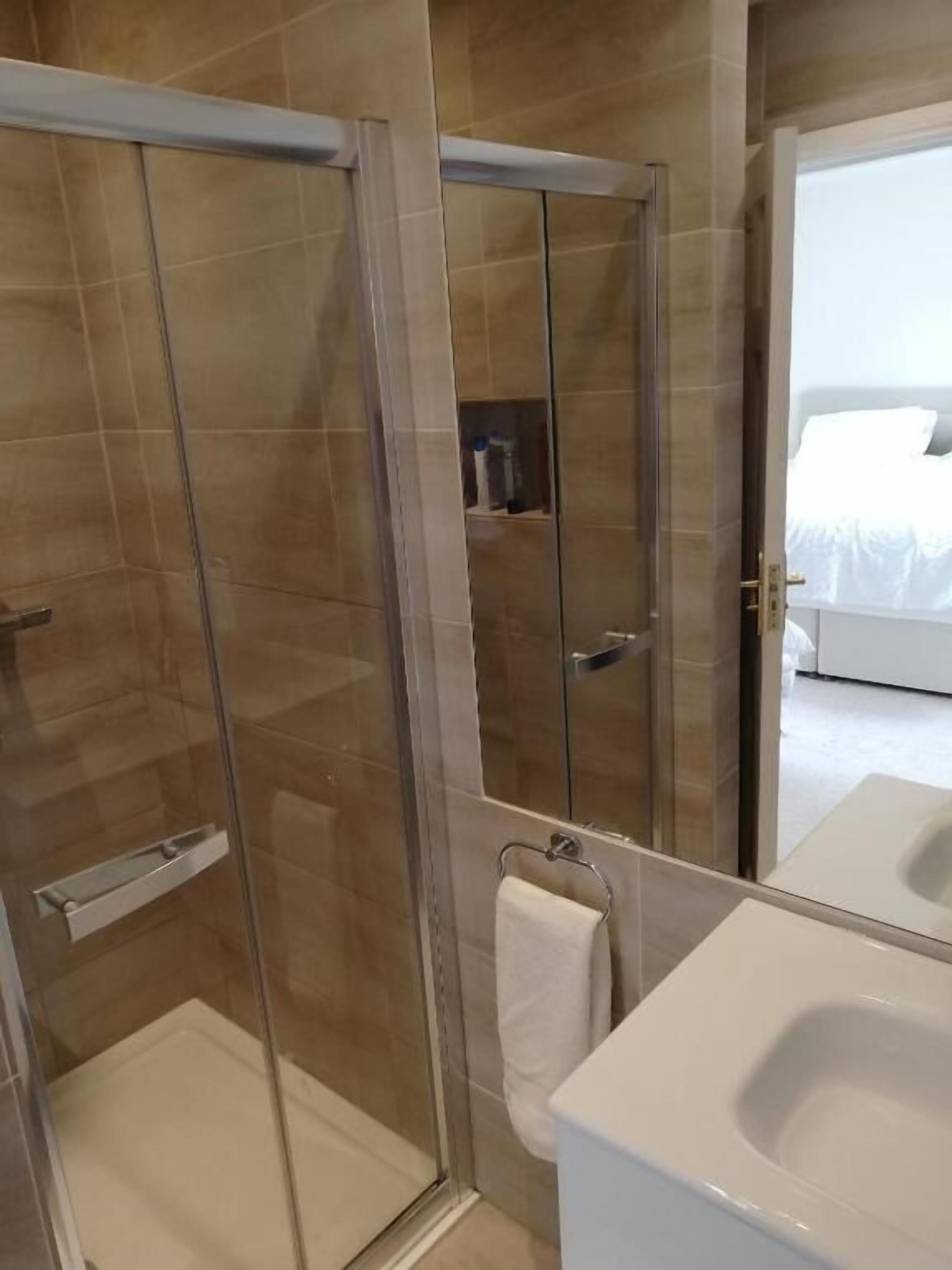 A modern bathroom with a glass-enclosed shower, a white sink, and a visible towel rack.