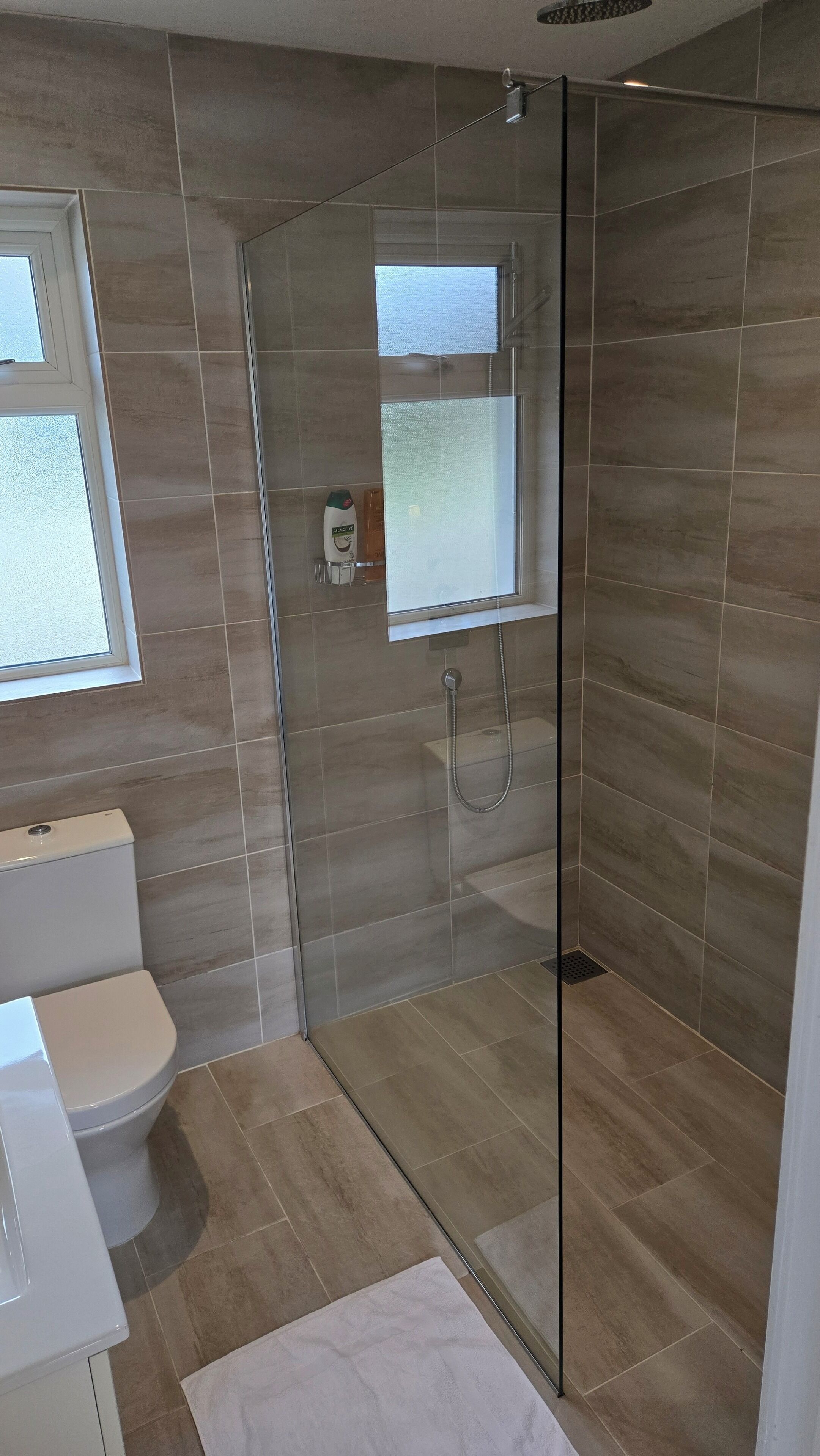 A modern bathroom with a glass-enclosed shower, a toilet, and a window providing natural light.