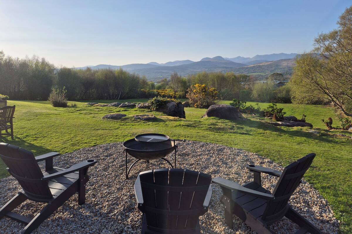 A patio with Adirondack chairs, a grill, and a view of mountains.