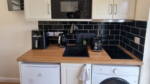 A compact kitchen with white cabinets, a microwave, a coffee maker, a toaster, and a washing machine. - Misty Bay (Dawros)