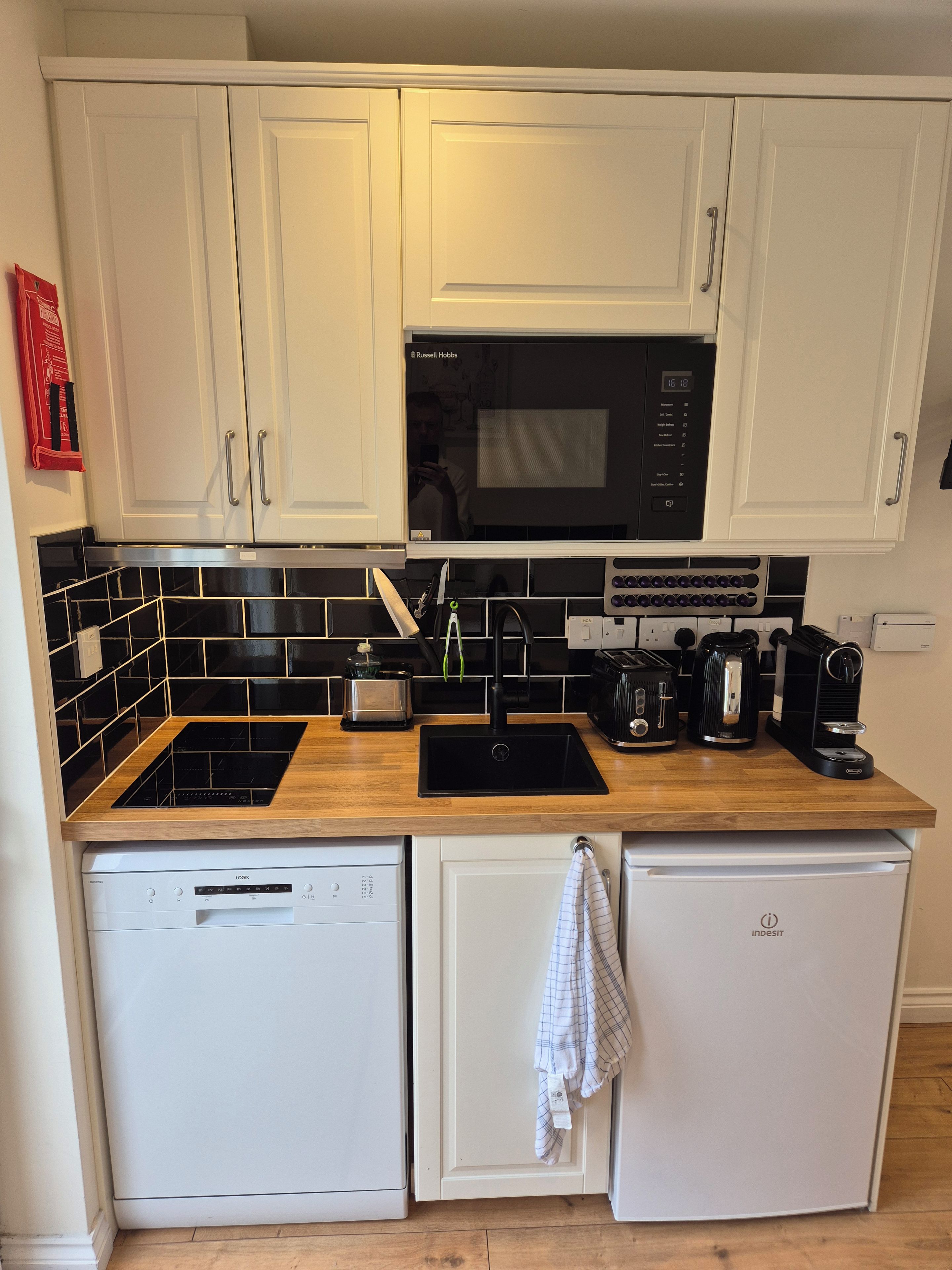 A compact kitchen with white cabinets, a black microwave, a coffee maker, and a dishwasher.