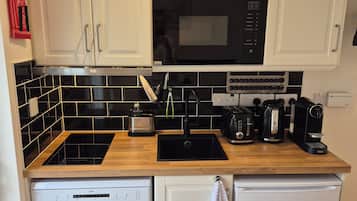 A compact kitchen with white cabinets, a black microwave, a coffee maker, and a dishwasher.
