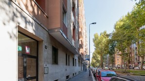 Une vue de rue avec des voitures garées, un trottoir et des immeubles à plusieurs étages dotés de balcons.