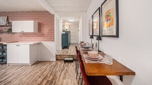 Moderni keittiö, jossa on valkoiset kaapit, tiilestä tehty korosteseinä ja ruokailutila, jossa on puinen pöytä ja neljä tuolia.