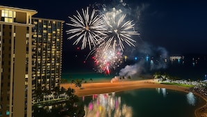 A beachfront hotel with a pool reflecting colorful lights, a beach, and a city skyline in the background. - @ Marbella Lane Dreamy Sunset Views by the Sea (Honolulu)