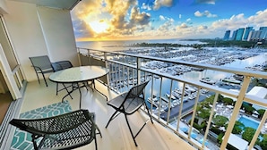 A balcony with a table and chairs, overlooking a marina with boats and a cityscape. - @ Marbella Lane Dreamy Sunset Views by the Sea (Honolulu)