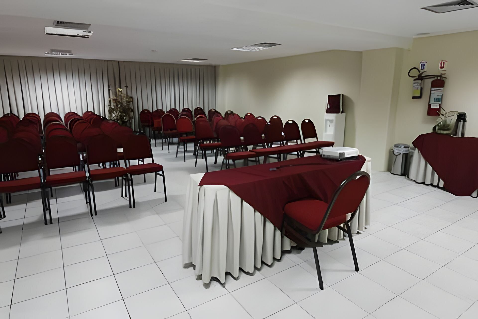 A conference room with rows of red chairs, a white table with a red tablecloth, and a white curtain backdrop.