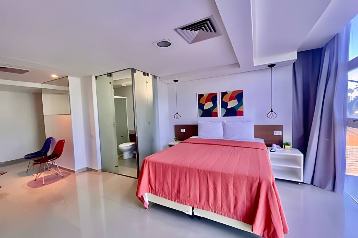 A modern hotel room with a bed, a desk, a chair, and a bathroom.