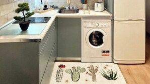 Eine kompakte Küche mit weißen Schränken, einer Mikrowelle, einer Waschmaschine und einem Kühlschrank.
