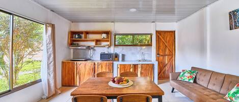 A modern kitchen with wooden cabinets, a dining table with chairs, and a sofa with cushions.