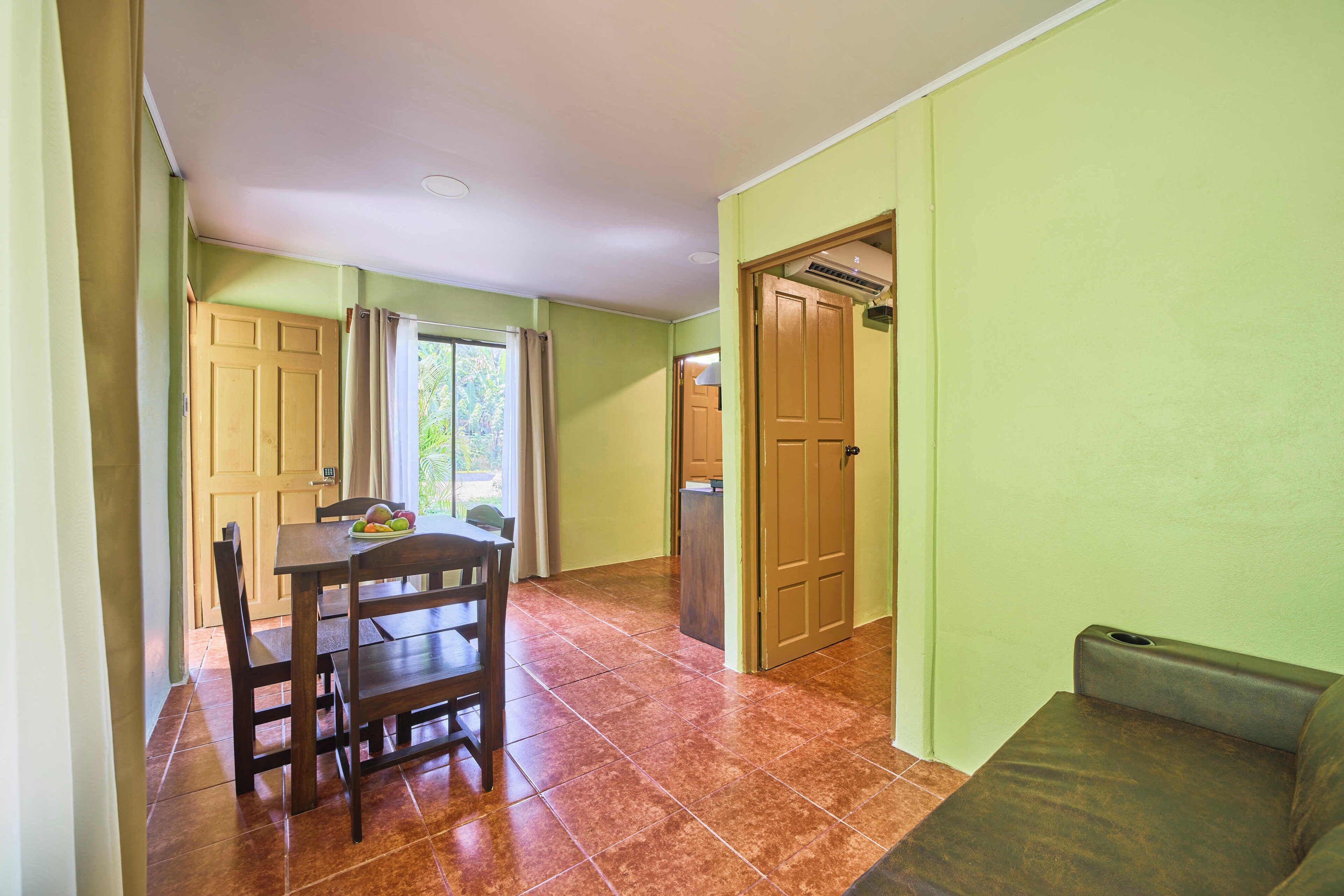A dining area with a wooden table and chairs, a sofa, and a door leading to another room.