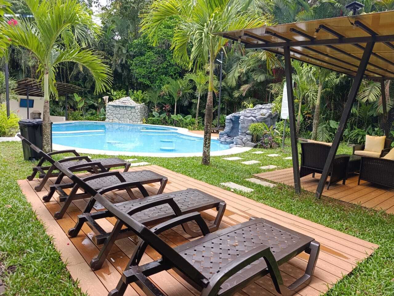 Un área junto a la piscina con sillones de descanso, una terraza de madera y una estructura de piedra.