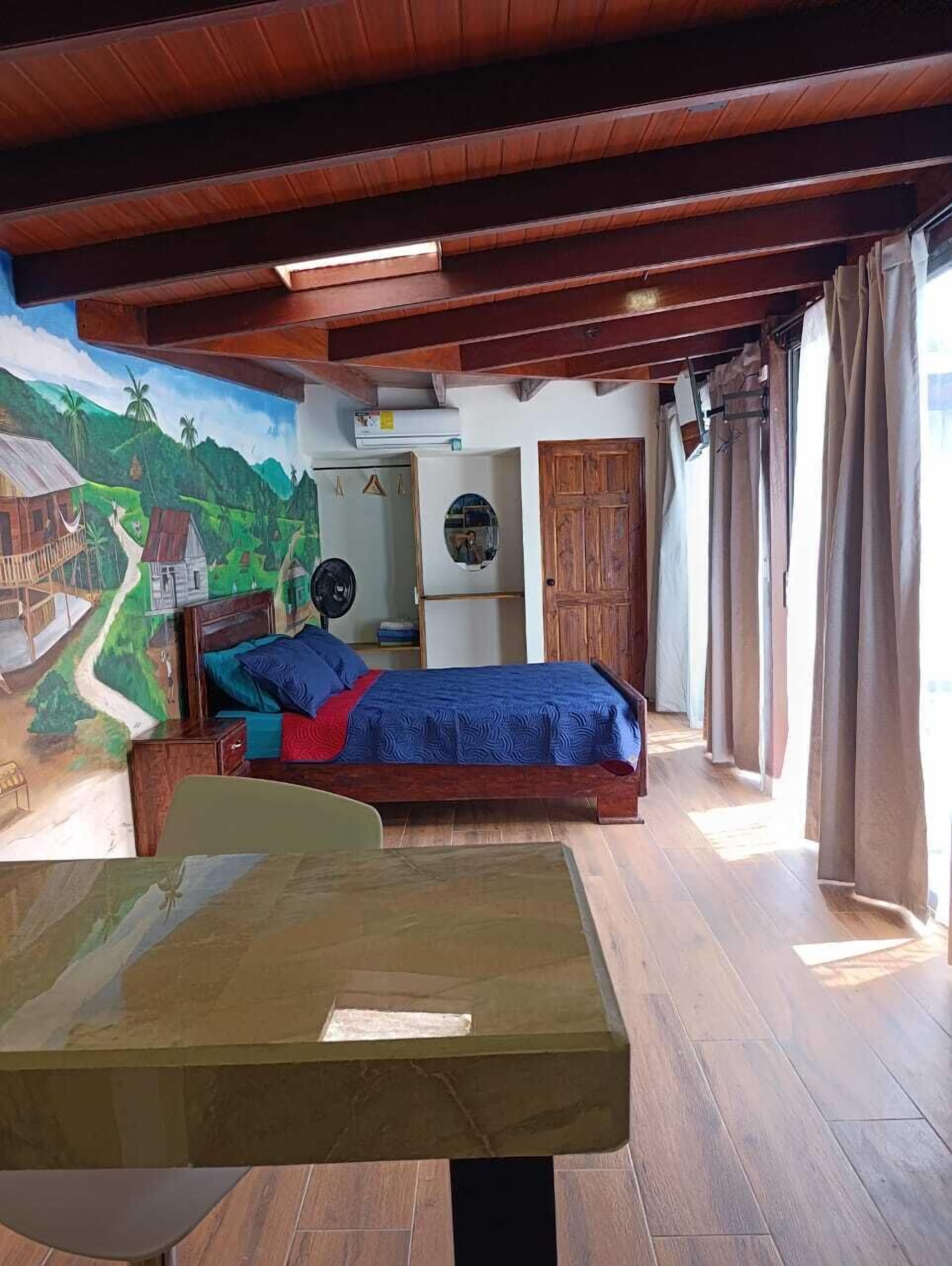 Une pièce avec un lit, une table, une fresque murale et une porte.