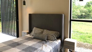 Un dormitorio con una cama grande, un aire acondicionado, una lámpara colgante y vistas a la vegetación exterior.