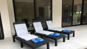 Tres sillones de exterior con cojines, ubicados en un patio con una puerta de vidrio al fondo.