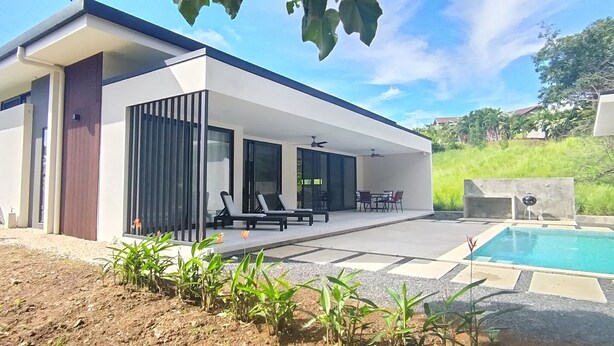 Una casa moderna con piscina, mobiliario de exterior y jardín.