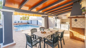 Une terrasse extérieure avec une piscine, une table et des chaises, ainsi qu’un espace barbecue.