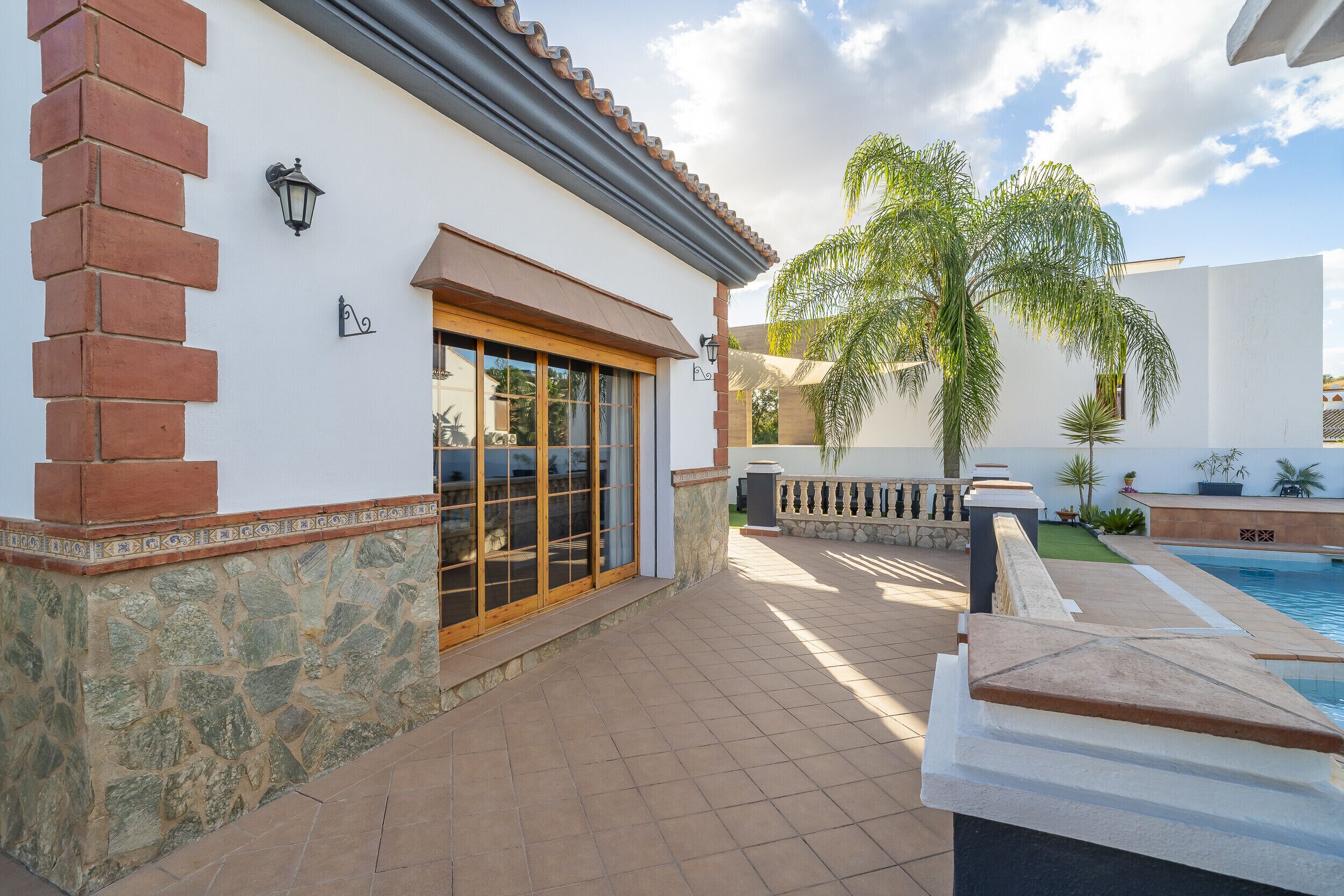 A patio area with a pool, stone walls, and a palm tree.