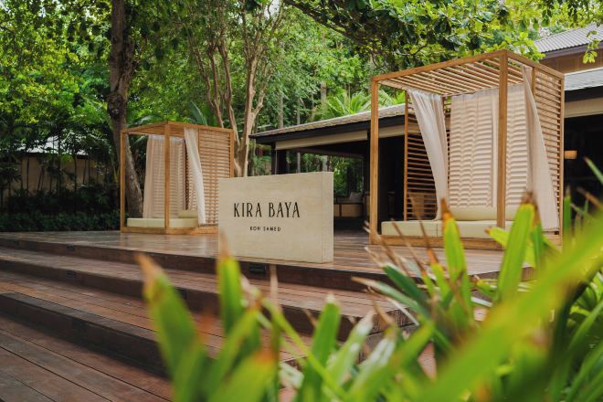 Eine Holzterrasse mit einem Schild, auf dem 'KIRA BAYA' steht, und einem überdachten Sitzbereich.