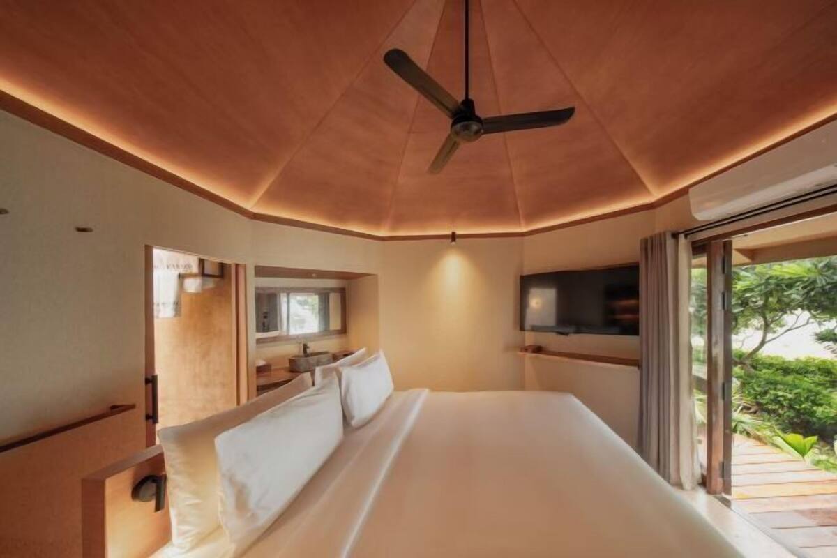 Un dormitorio moderno con una cama grande, ventilador de techo y vistas a zonas verdes.