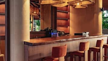 Een bar met een houten toonbank, barstoelen en hangende lampen.