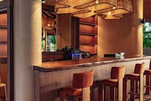 Een bar met een houten toonbank, barstoelen en hangende lampen.