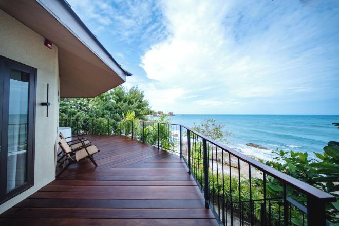 Eine Holzterrasse mit Geländer, mit Blick auf einen Strand und den Ozean.