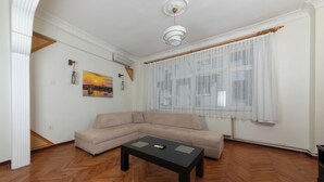 A living room with a beige sectional sofa, a black coffee table, and a painting on the wall. - In the Center of Ancient Lands-2 (İstanbul)