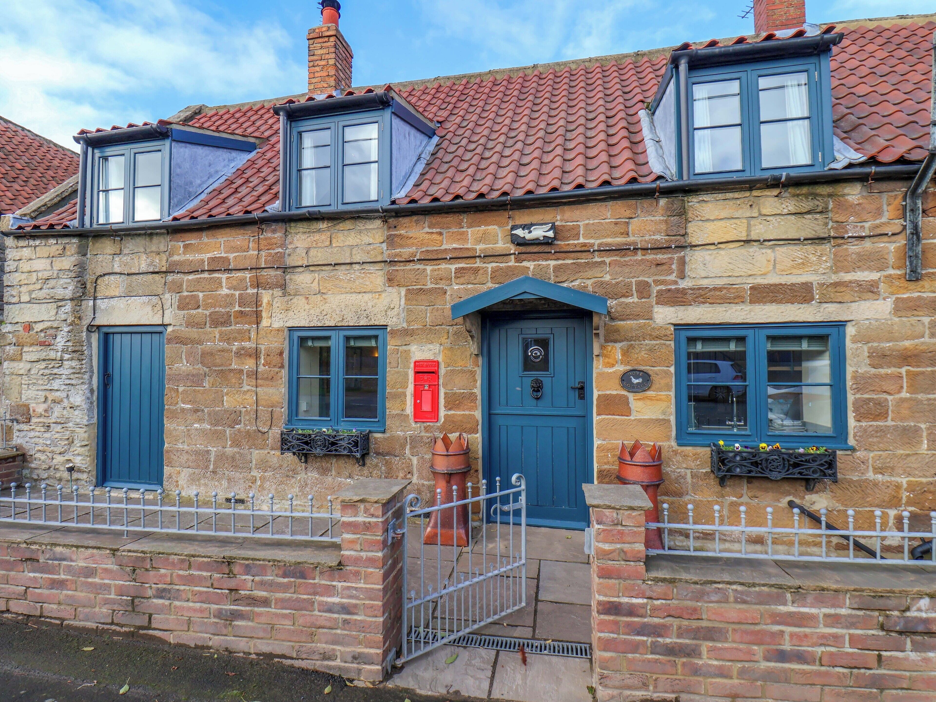 A stone building with a blue door, two windows with blue shutters, and a red mailbox.