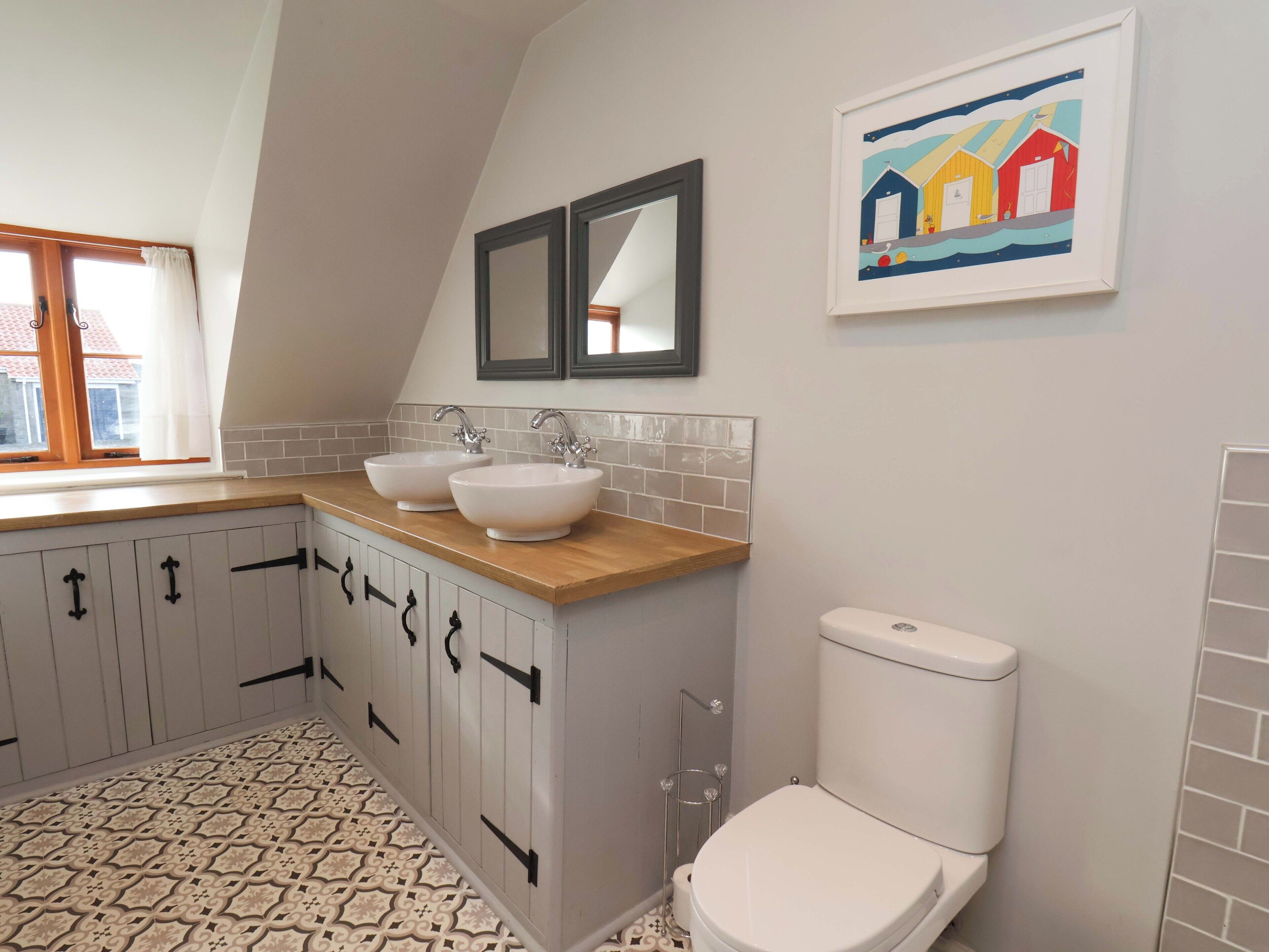 Une salle de bain avec deux lavabos, des toilettes, une fenêtre et un tableau au mur.