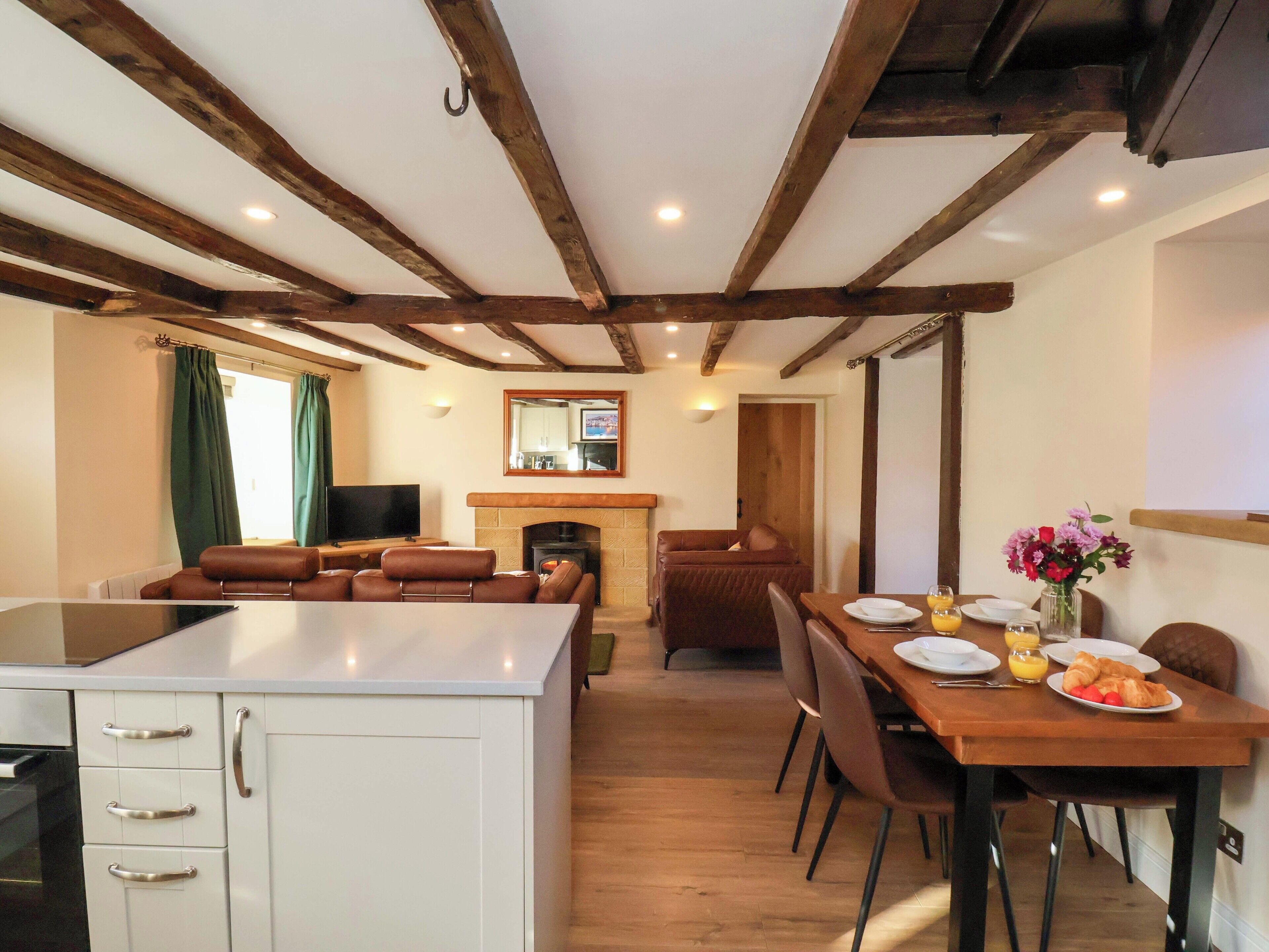 A dining area with a wooden table, chairs, and a fireplace. There is a kitchen area with cabinets and a television.