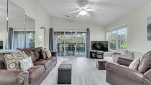 A spacious living room with a large brown leather sofa, a white sofa, and a black ottoman. There is a flat-screen TV on a stand, and a ceiling fan above. - Peaceful 2BR Condo by Golf Course & Pools (Branson)