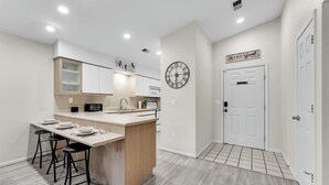 A modern kitchen with a central island, bar stools, a clock, and a sign that reads "BE OUR GUEST". - Peaceful 2BR Condo by Golf Course & Pools (Branson)