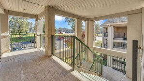 A covered outdoor area with concrete pillars, a metal railing, and a view of a parking lot and buildings. - Peaceful 2BR Condo by Golf Course & Pools (Branson)