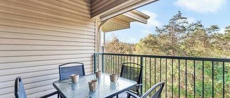 A covered patio with a table and chairs, a railing, and a view of trees and sky.