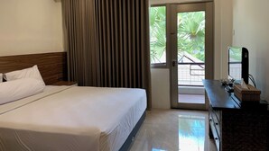 Une chambre d’hôtel comprenant un lit, une commode, un miroir et une porte donnant sur un balcon avec vue sur la verdure.