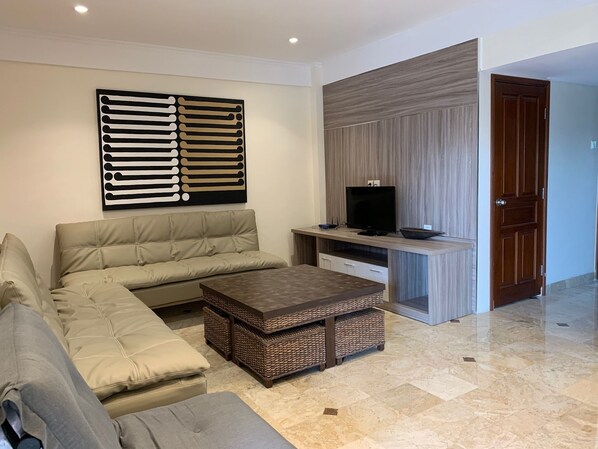 Una sala moderna con un sofá seccional, una mesa de centro, un televisor de pantalla plana y un adorno de pared.