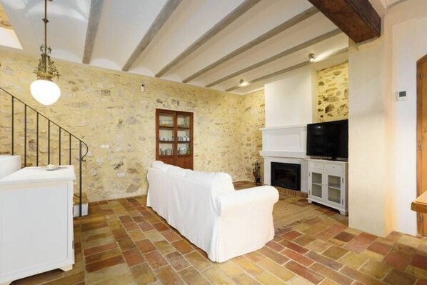 A stone-walled living room with a white sofa, a fireplace, and a television. - Mira Altea - A Luxurious Boutique Stay (Altea)
