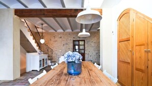 Ein Essbereich mit Holztisch, weißen Stühlen, einem Blumenstrauß, einer Treppe und einer Holztür.