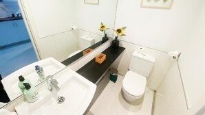 Et moderne badeværelse med en hvid vask, to spejle, et toilet og en lille skraldespand.