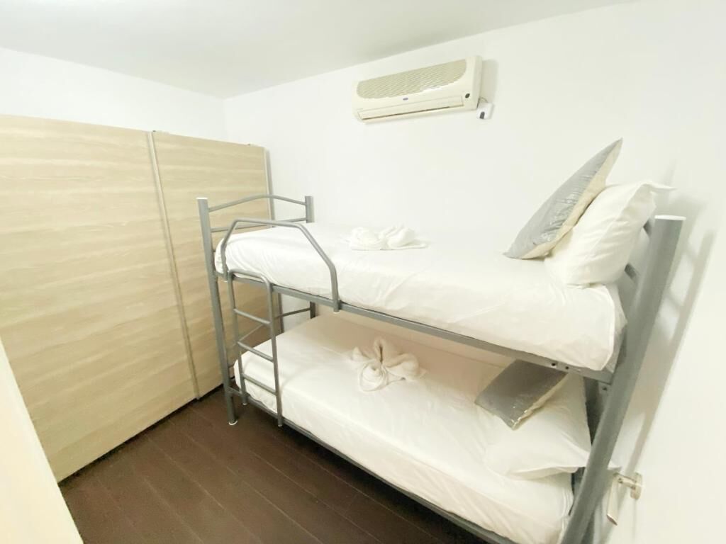 Habitación con literas, un armario de madera, un equipo de aire acondicionado blanco y una escalera metálica.