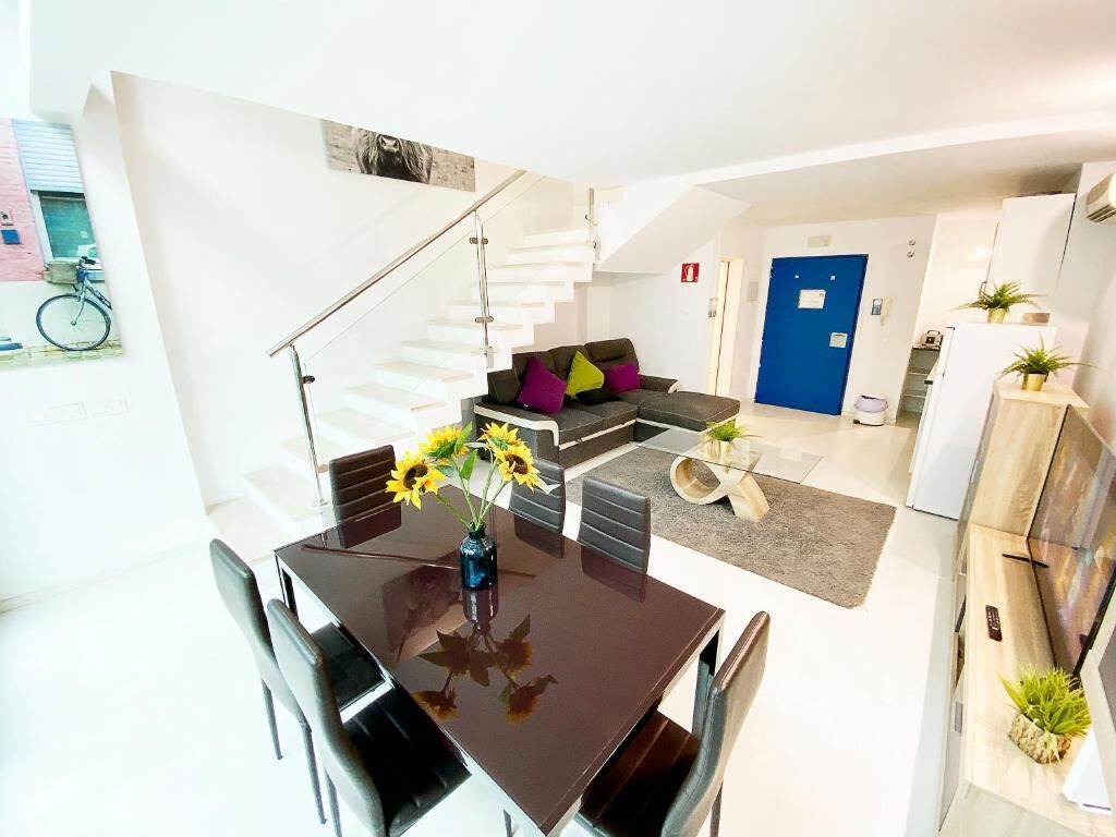 A modern living space with a dining area, sofa, staircase, and kitchen.