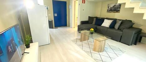 Una sala de estar moderna con un televisor de pantalla plana, un sofá, una mesa de centro y una escalera.