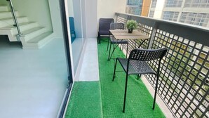 En balkon med kunstgræs, to stole, et lille bord og en potteplante.