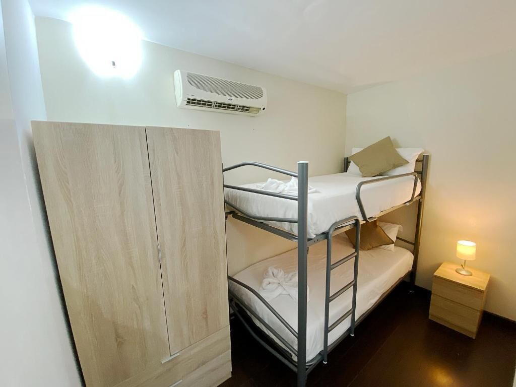 A bunk bed room with a wardrobe, a bedside table with a lamp, and an air conditioning unit on the wall.