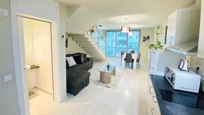 Et moderne køkken med spiseplads, en trappe til en balkon og en stue med sofa og sofabord.