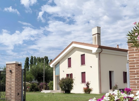 A two-story building with a brick chimney, a small attached garage, and a well-maintained lawn with flowering plants.. Mobile Home 'Casa Oleandro 2' with Private Garden, Wi-Fi and Air Conditioning