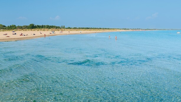 Una playa con agua cristalina, orilla de arena y algunas personas.